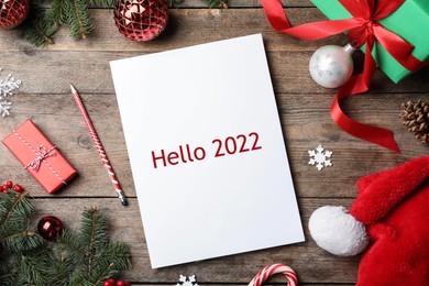 Paper with text Hello 2022 and Christmas decor on wooden table, flat lay
