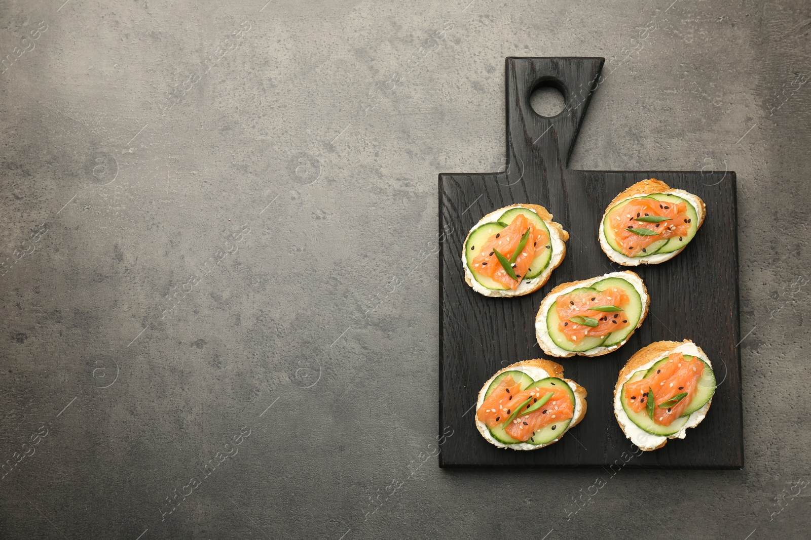 Photo of Tasty canapes with salmon, cucumber and cream cheese on grey table, top view. Space for text