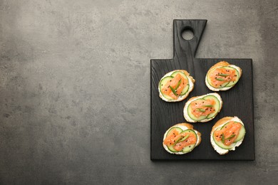 Photo of Tasty canapes with salmon, cucumber and cream cheese on grey table, top view. Space for text