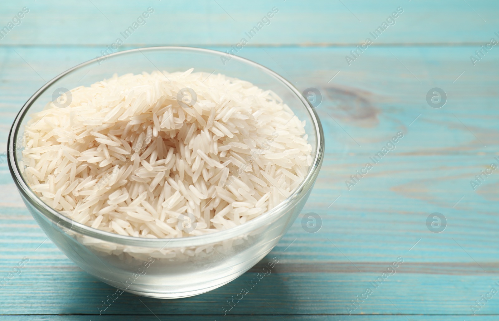 Photo of Raw basmati rice in bowl on light blue wooden table, closeup. Space for text