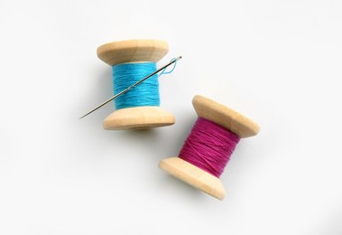 Colorful sewing threads with needle on white background, top view