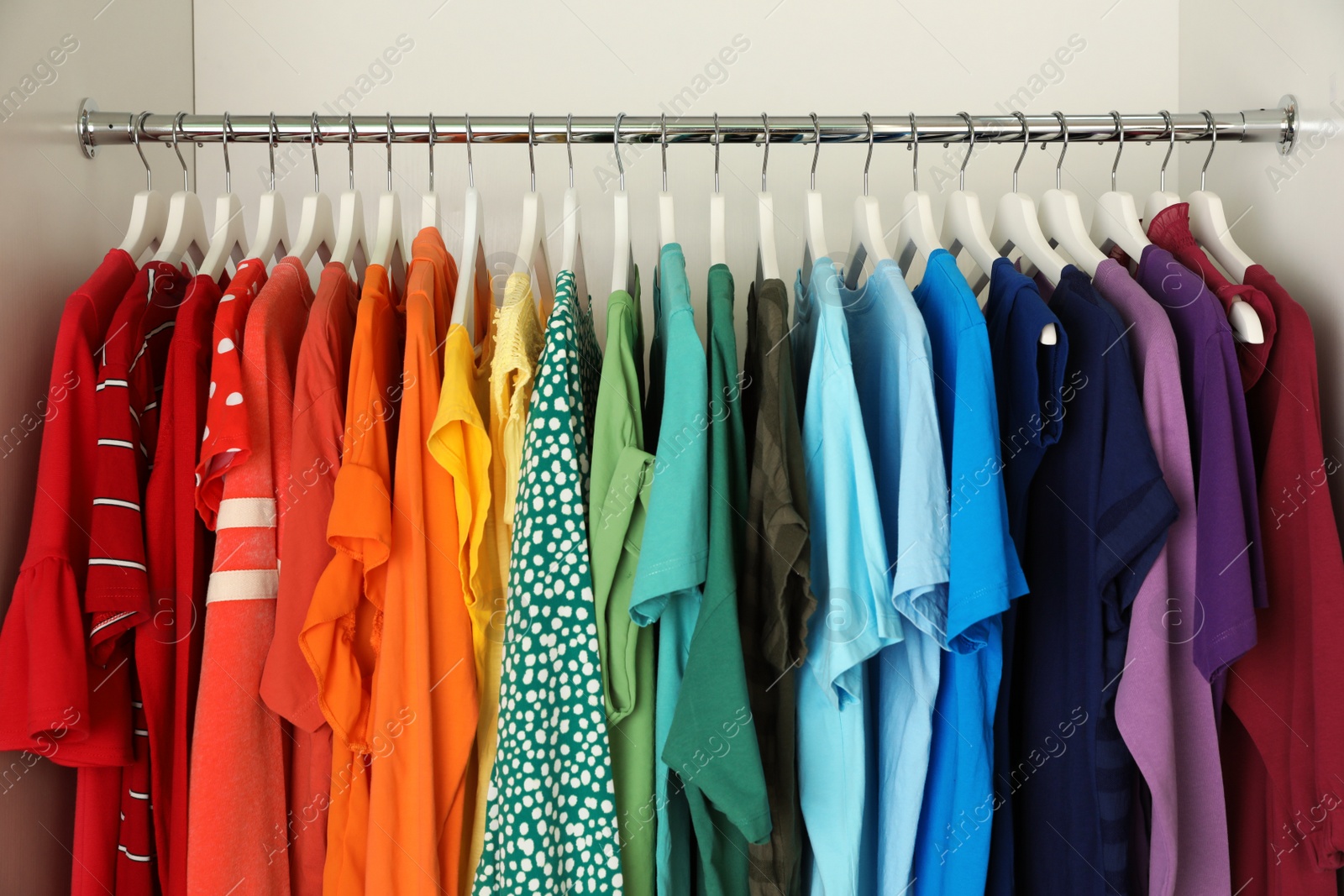 Photo of Hangers with different colorful clothes on rack in wardrobe