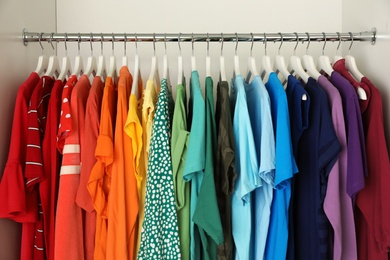 Hangers with different colorful clothes on rack in wardrobe