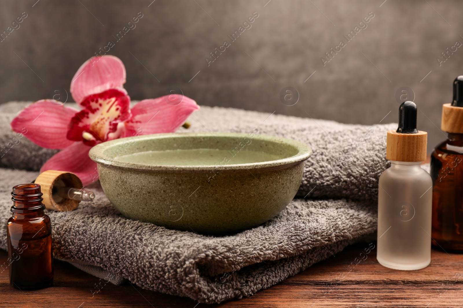 Photo of Bowl of essential oil and beautiful flower on wooden table. Aromatherapy treatment