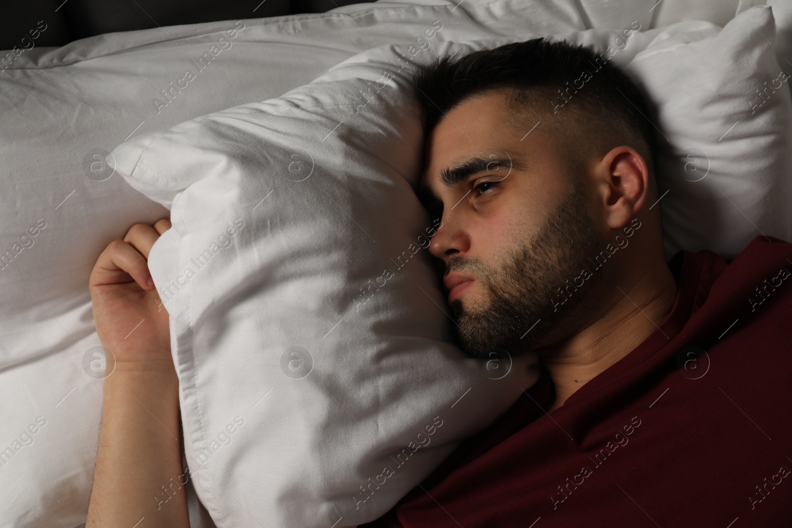 Photo of Sad man lying on bed at home, top view