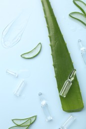 Flat lay composition with skincare ampoules and aloe leaves on light blue background