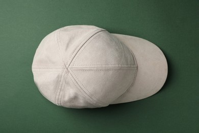 Stylish beige baseball cap on dark green background, top view