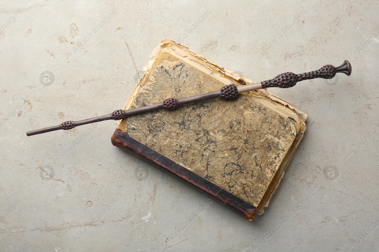 Photo of Magic wand and old book on light textured background, top view