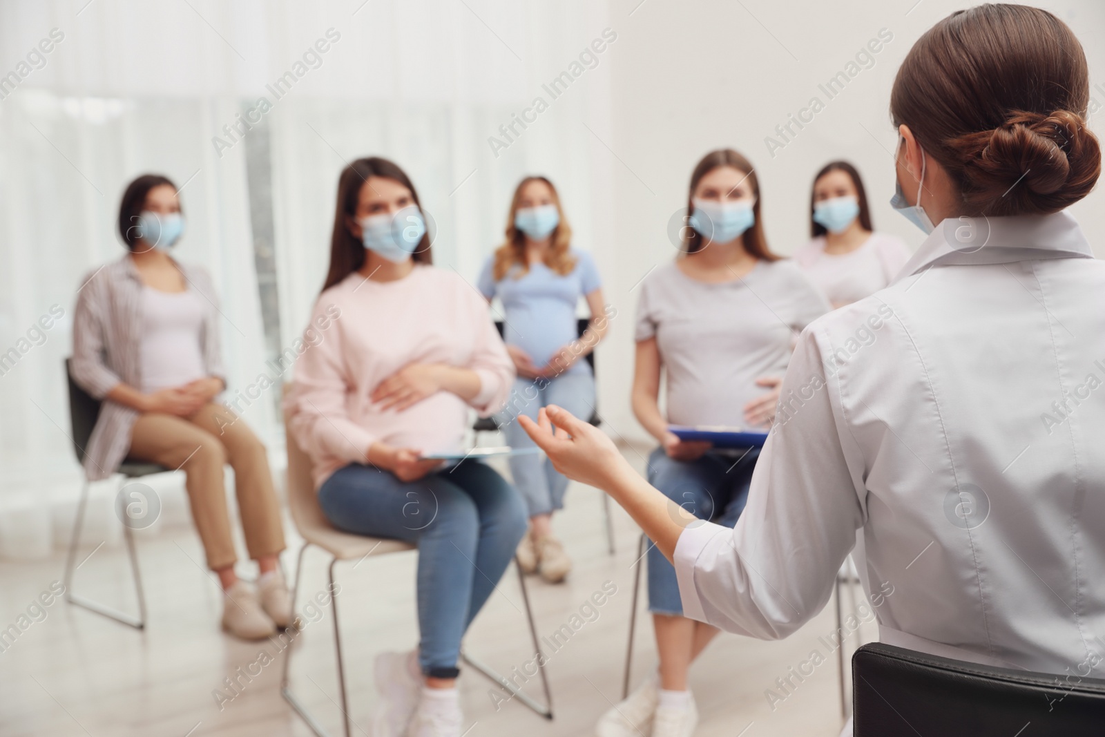 Photo of Group of pregnant women in protective masks with doctor at courses for expectant mothers indoors