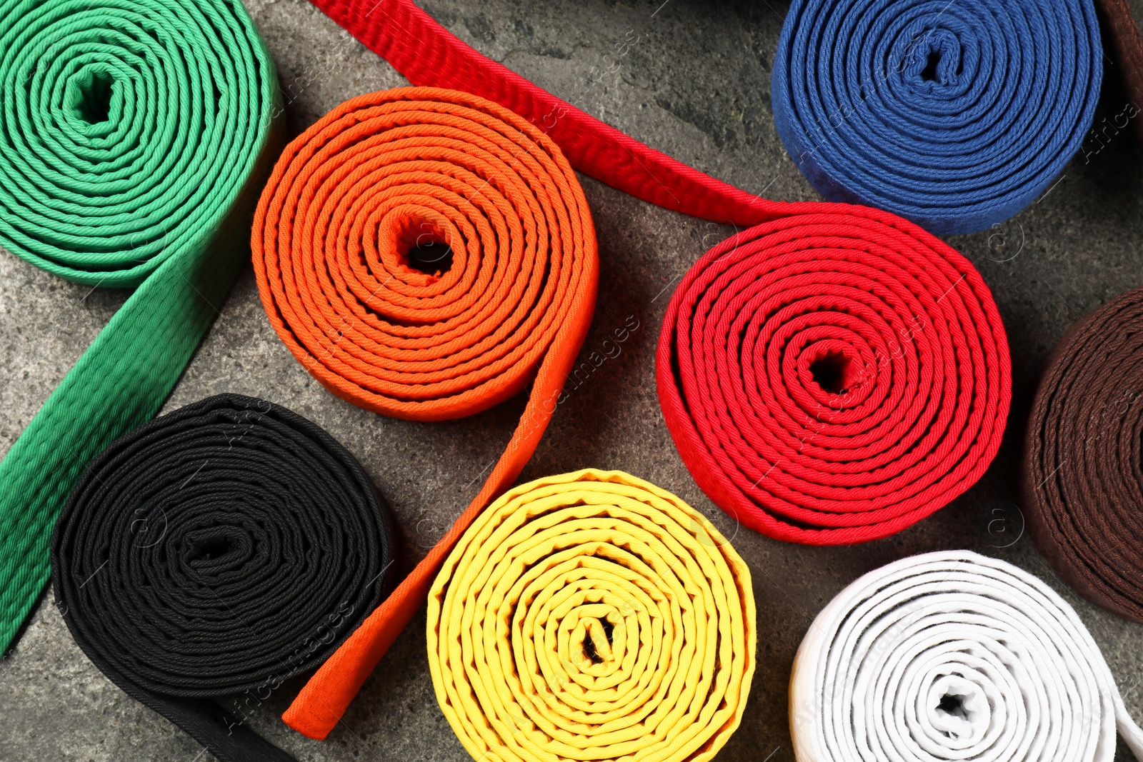 Photo of Colorful karate belts on gray background, flat lay