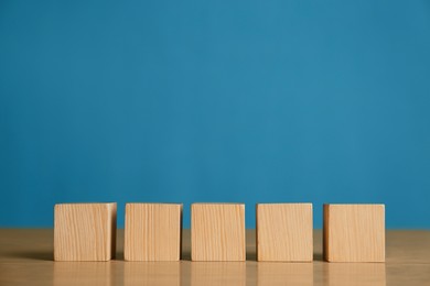 Photo of Row of blank cubes on wooden table against light blue background. Space for text