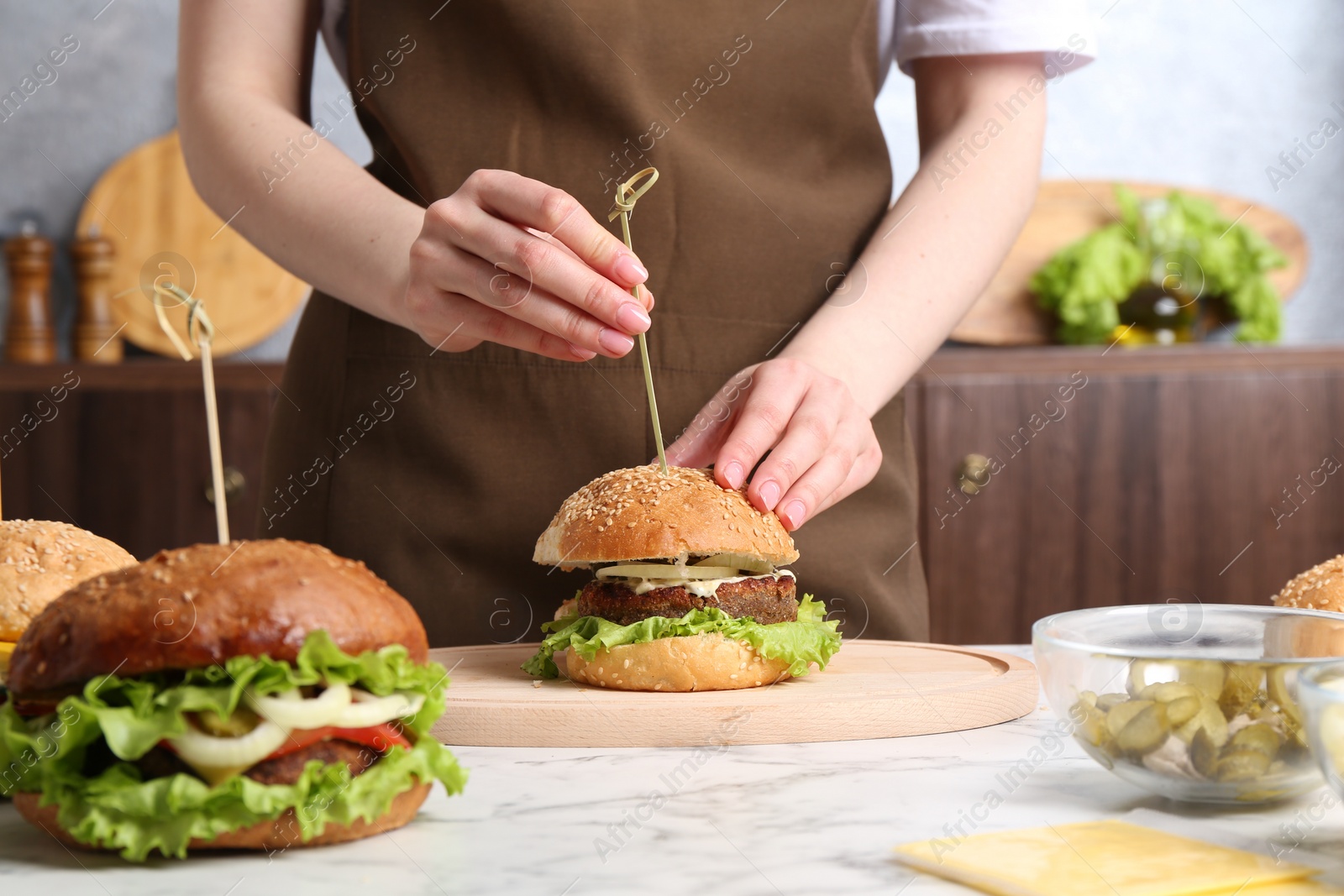 Photo of Woman making delicious vegetarian burger at white marble table, closeup