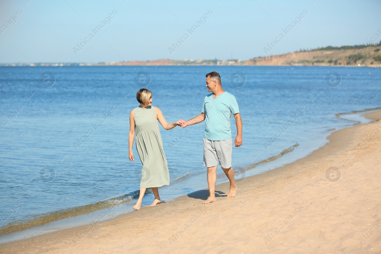 Photo of Happy mature couple holding hands at beach on sunny day