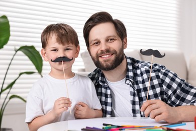 Happy dad and son with paper mustaches at home