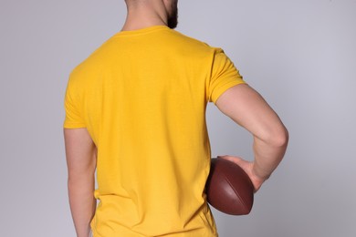 Photo of Athletic man with American football ball on light grey background, closeup