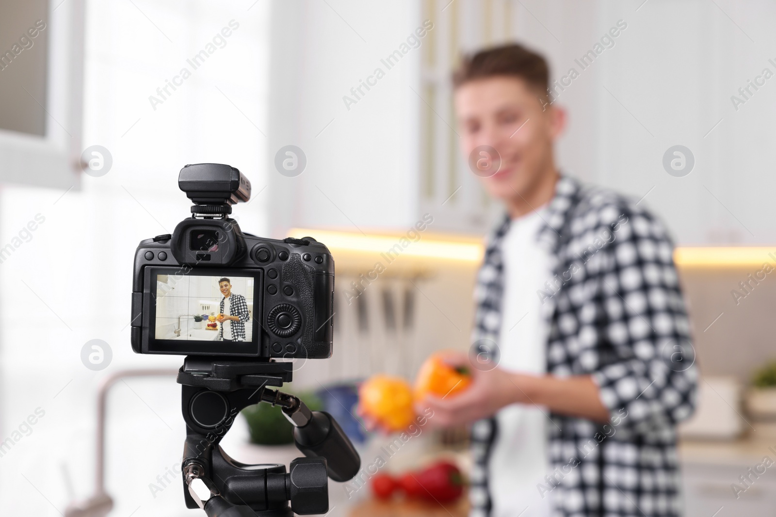 Photo of Food blogger recording video in kitchen, focus on camera