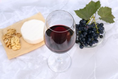Glass of red wine and snacks served on white marble table, above view