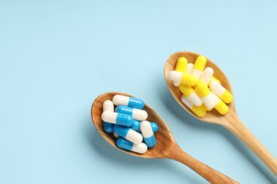 Photo of Antibiotic pills and spoons on light blue background, flat lay. Space for text