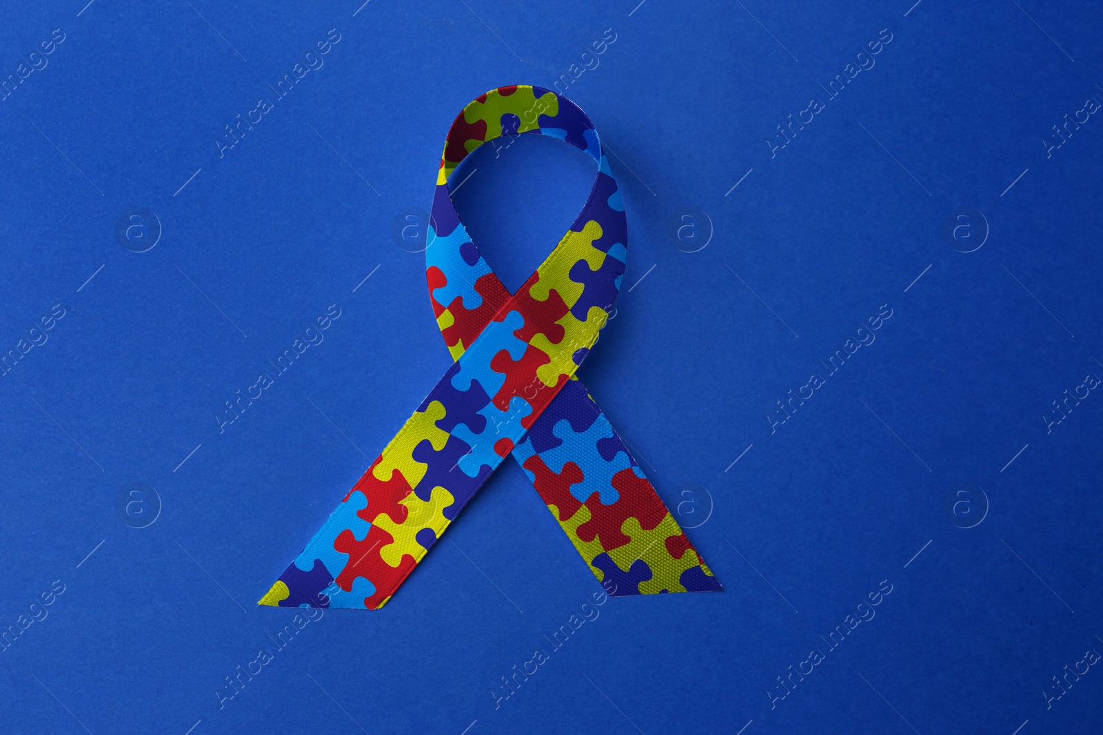 Image of World Autism Awareness Day. Colorful puzzle ribbon on blue background, top view