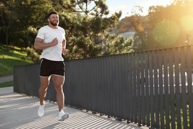 Photo of Young man running outdoors on sunny day. Space for text