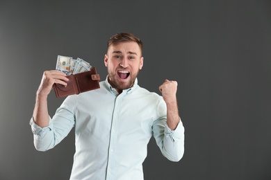 Photo of Emotional young man with wallet full of money on grey background. Space for text