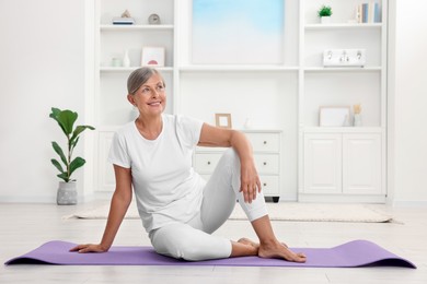 Happy senior woman sitting on mat at home. Yoga practice