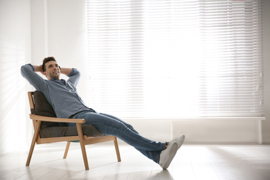 Photo of Young man relaxing in armchair near window at home. Space for text