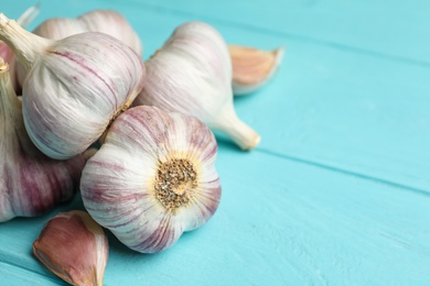 Photo of Fresh unpeeled garlic bulbs and cloves on light blue wooden table, closeup with space for text. Organic product