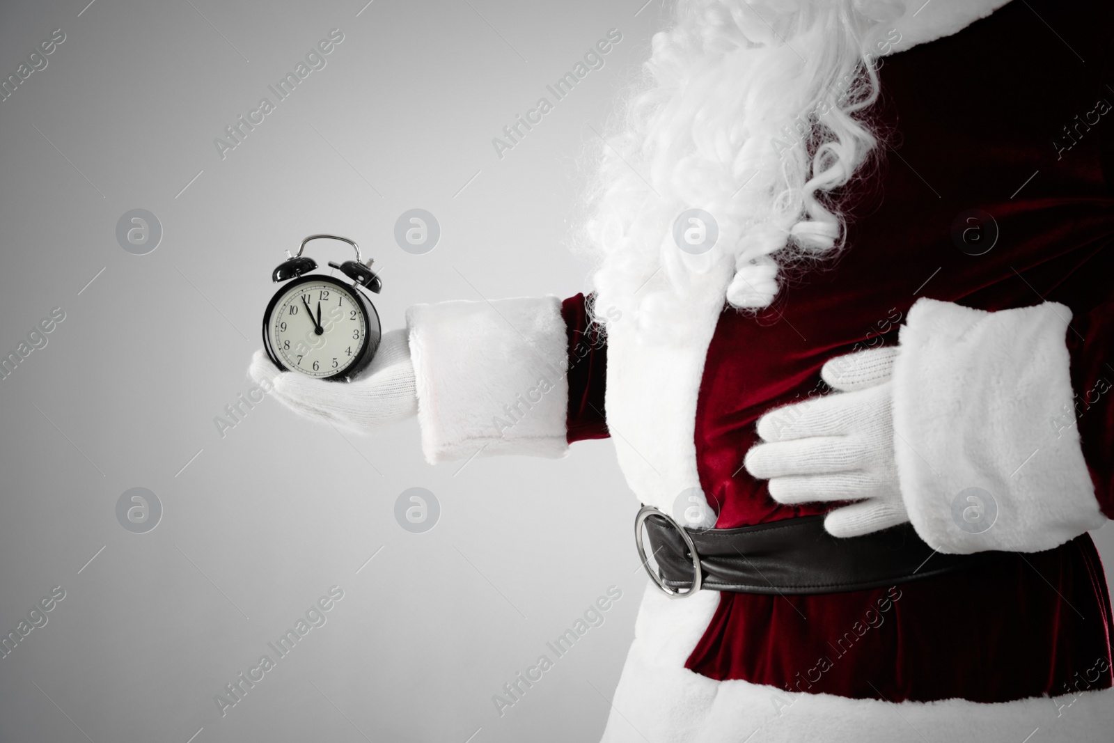 Photo of Santa Claus holding alarm clock on light grey background, closeup. Christmas countdown