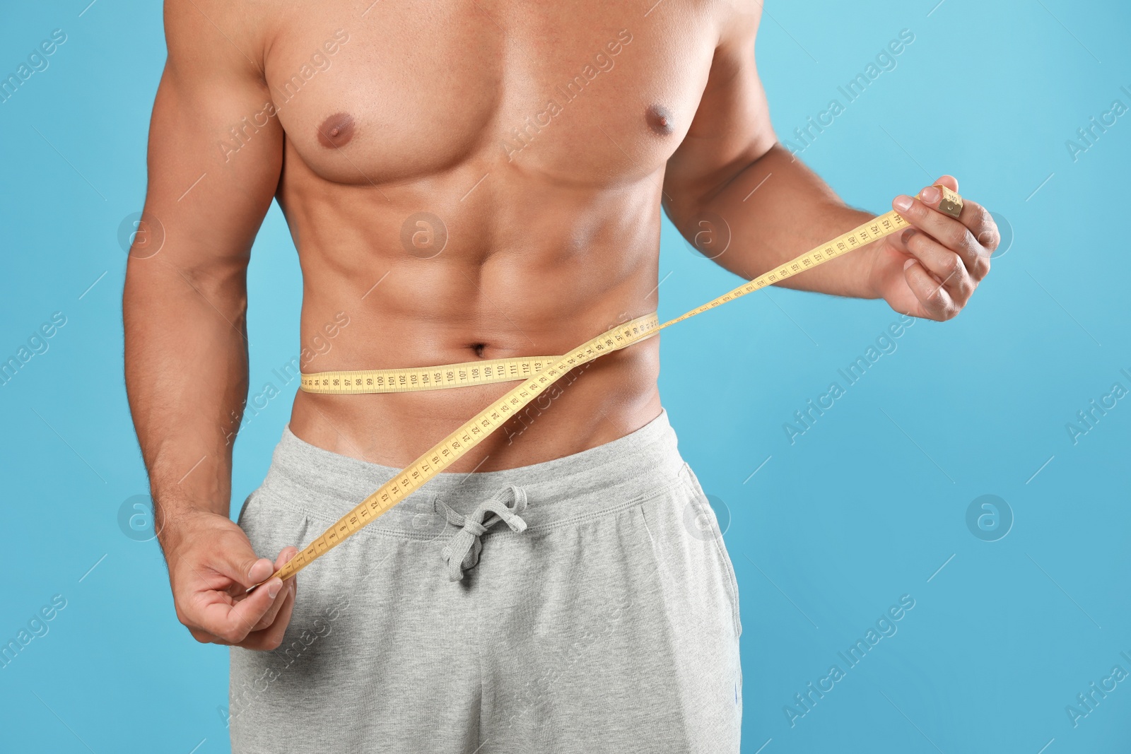 Photo of Young man with slim body using measuring tape on light blue background, closeup view