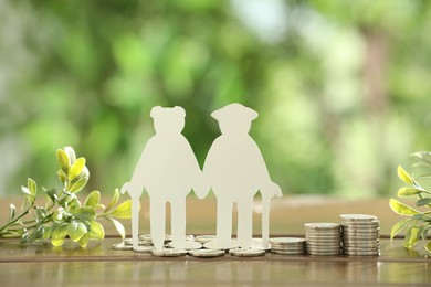 Photo of Pension savings. Figure of senior couple, coins and green twigs on wooden table outdoors