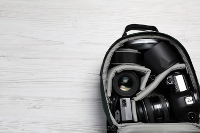 Photo of Professional photography equipment in backpack on white wooden table, top view. Space for text
