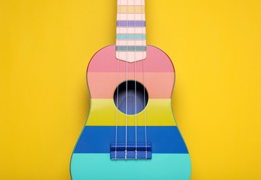 Colorful ukulele on yellow background, top view. String musical instrument