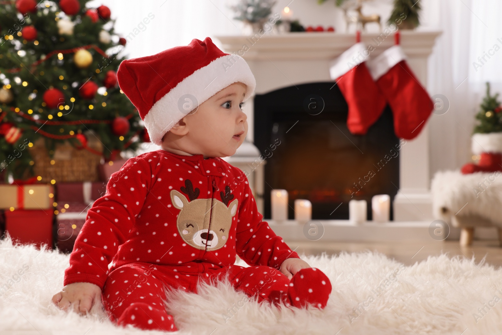 Photo of Baby in Santa hat and bright Christmas pajamas on floor at home