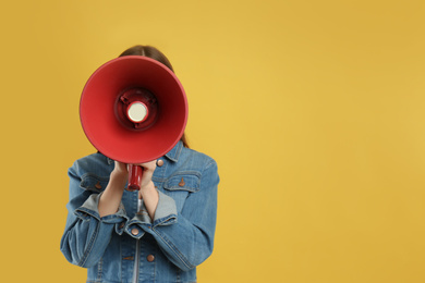 Young woman with megaphone on yellow background. Space for text