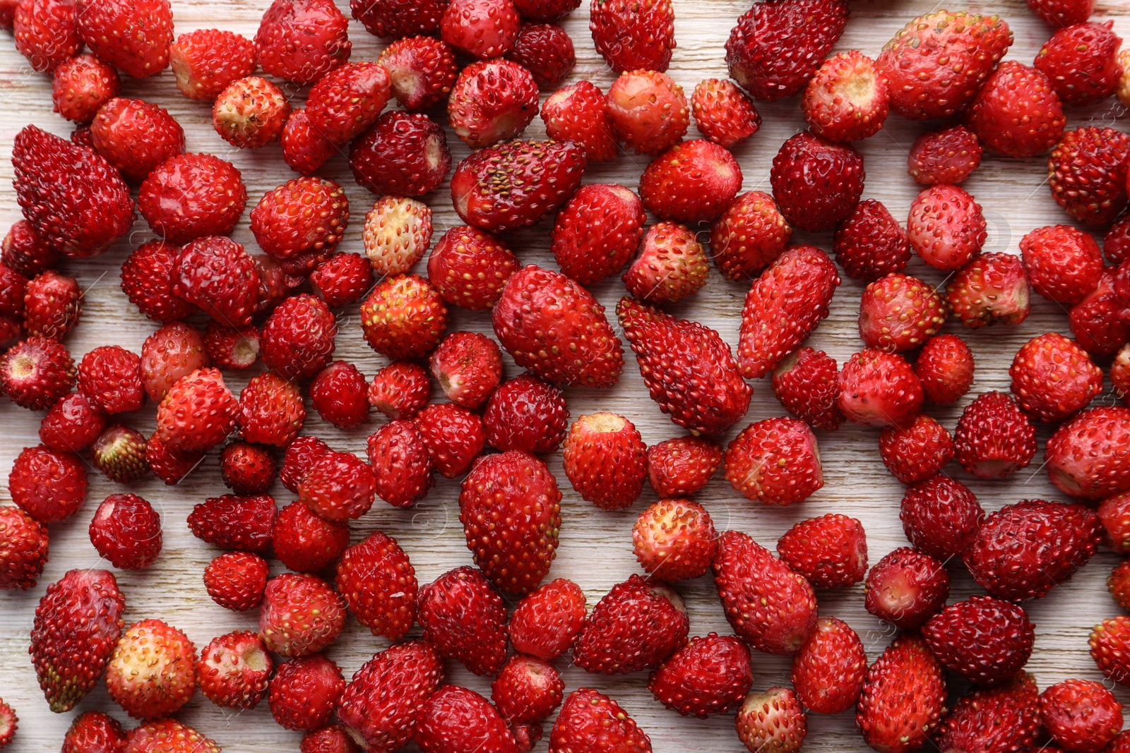 Photo of Many fresh wild strawberries on white wooden table, flat lay