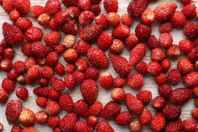 Many fresh wild strawberries on white wooden table, flat lay