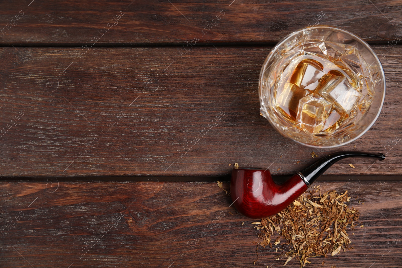 Photo of Classic smoking pipe with tobacco and glass of whiskey on wooden table, flat lay. Space for text