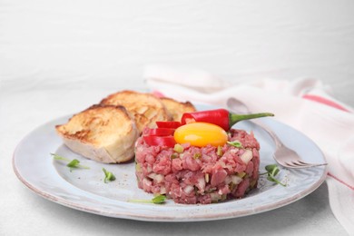 Photo of Tasty beef steak tartare served with yolk and other accompaniments on white table
