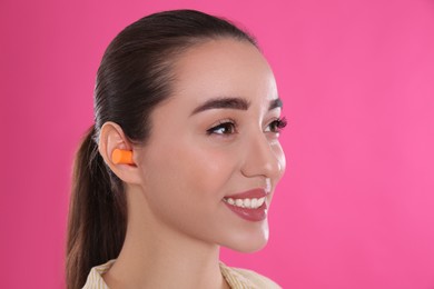 Young woman wearing foam ear plugs on pink background