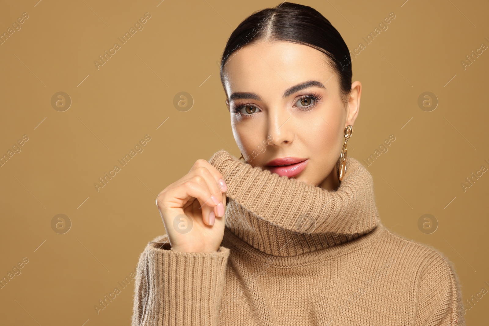 Photo of Beautiful young woman with elegant earrings on light brown background