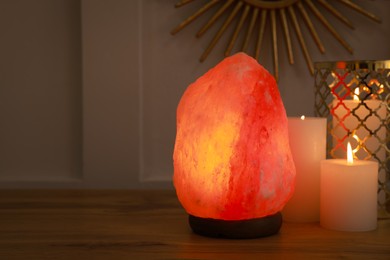 Himalayan salt lamp and candles on wooden table near white wall indoors, space for text