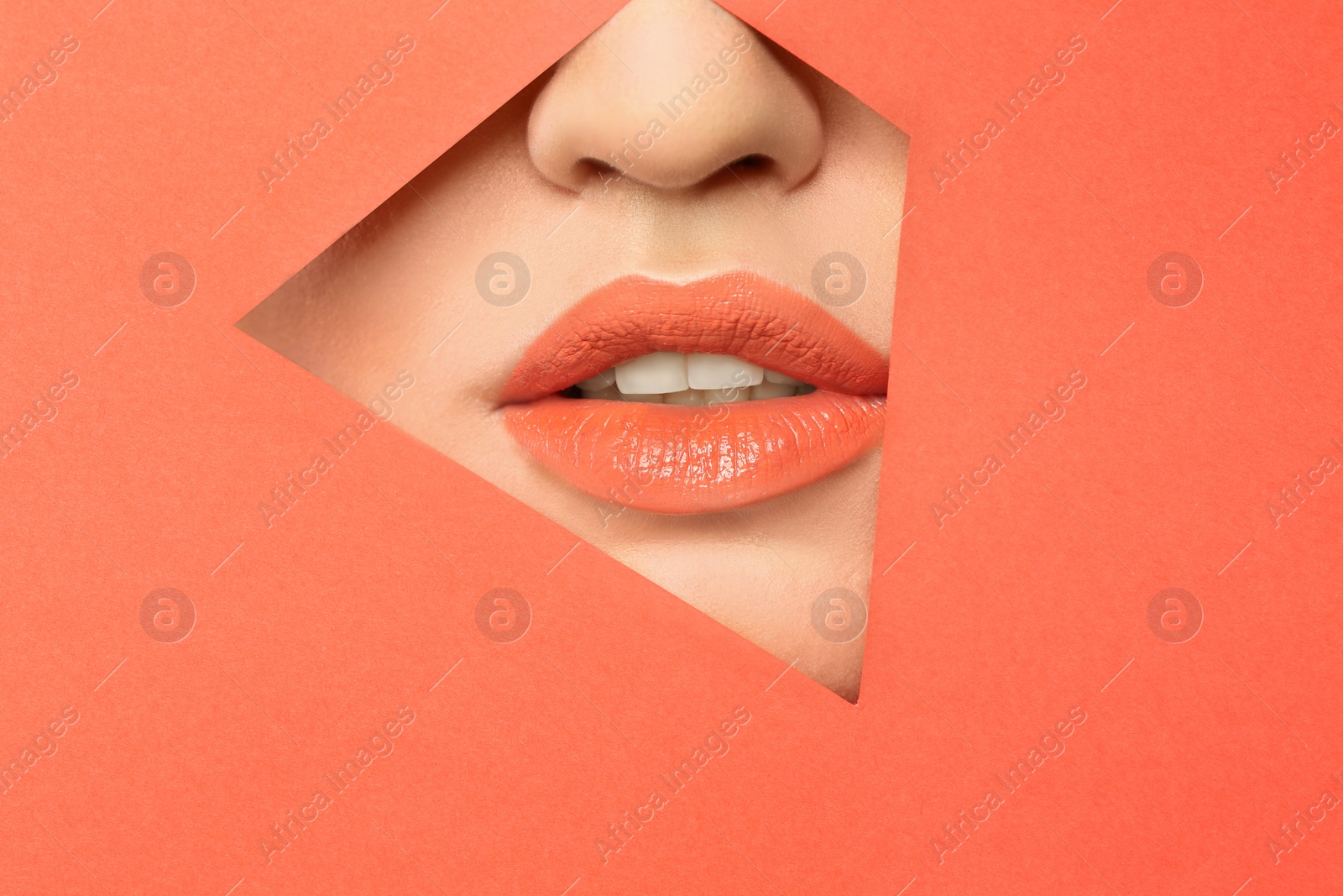 Photo of Lips of young woman with beautiful lipstick visible through hole in color paper