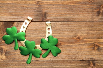 Photo of Golden horseshoe and decorative clover leaves on wooden table, flat lay with space for text. Saint Patrick's Day celebration