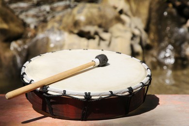 Photo of Drum with mallet near pond on sunny day, closeup. Percussion musical instrument