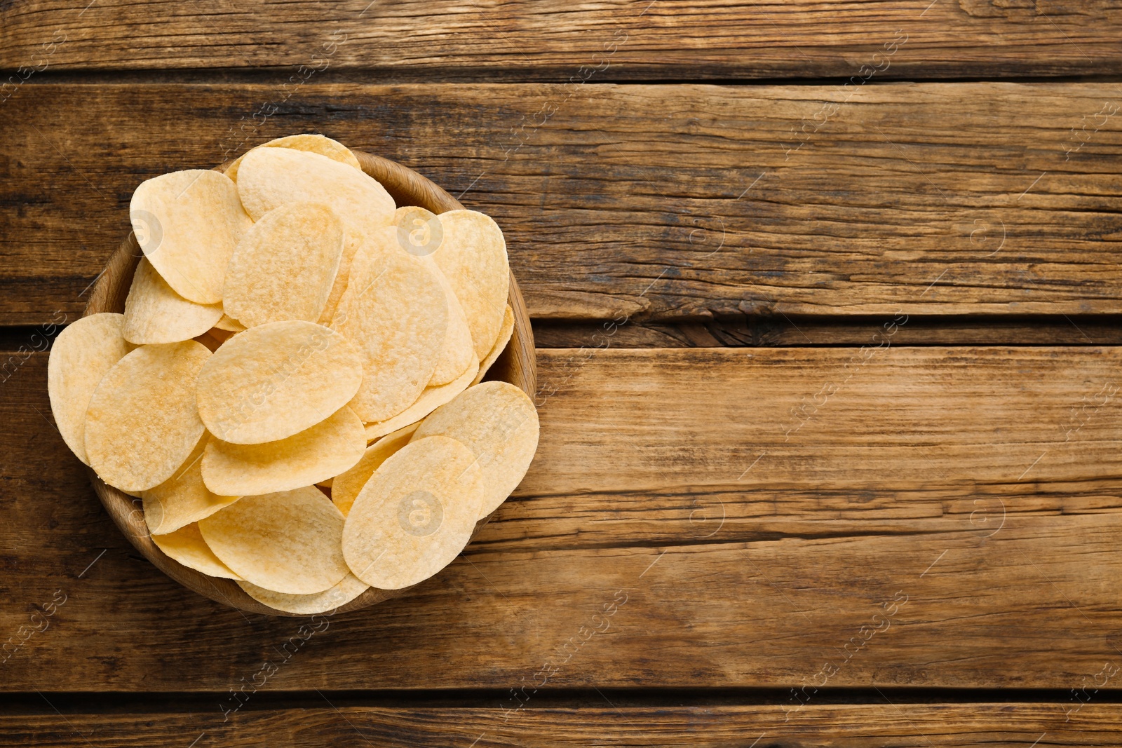 Photo of Bowl with delicious potato chips on wooden table, top view. Space for text