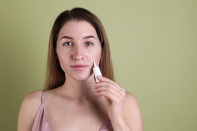 Photo of Young woman with acne problem applying cosmetic product onto her skin on olive background. Space for text