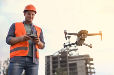 Builder operating drone with remote control at construction site, focus on quadcopter. Aerial survey