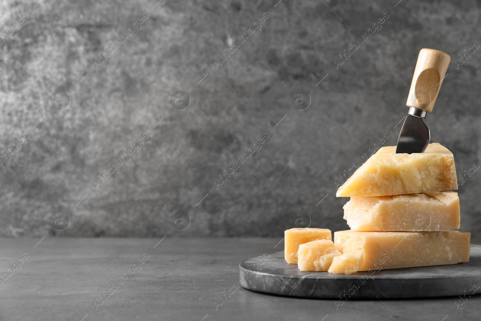 Photo of Parmesan cheese with board and knife on grey table. Space for text