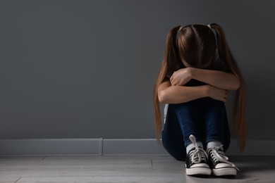 Sad girl sitting on floor near dark grey wall indoors, space for text